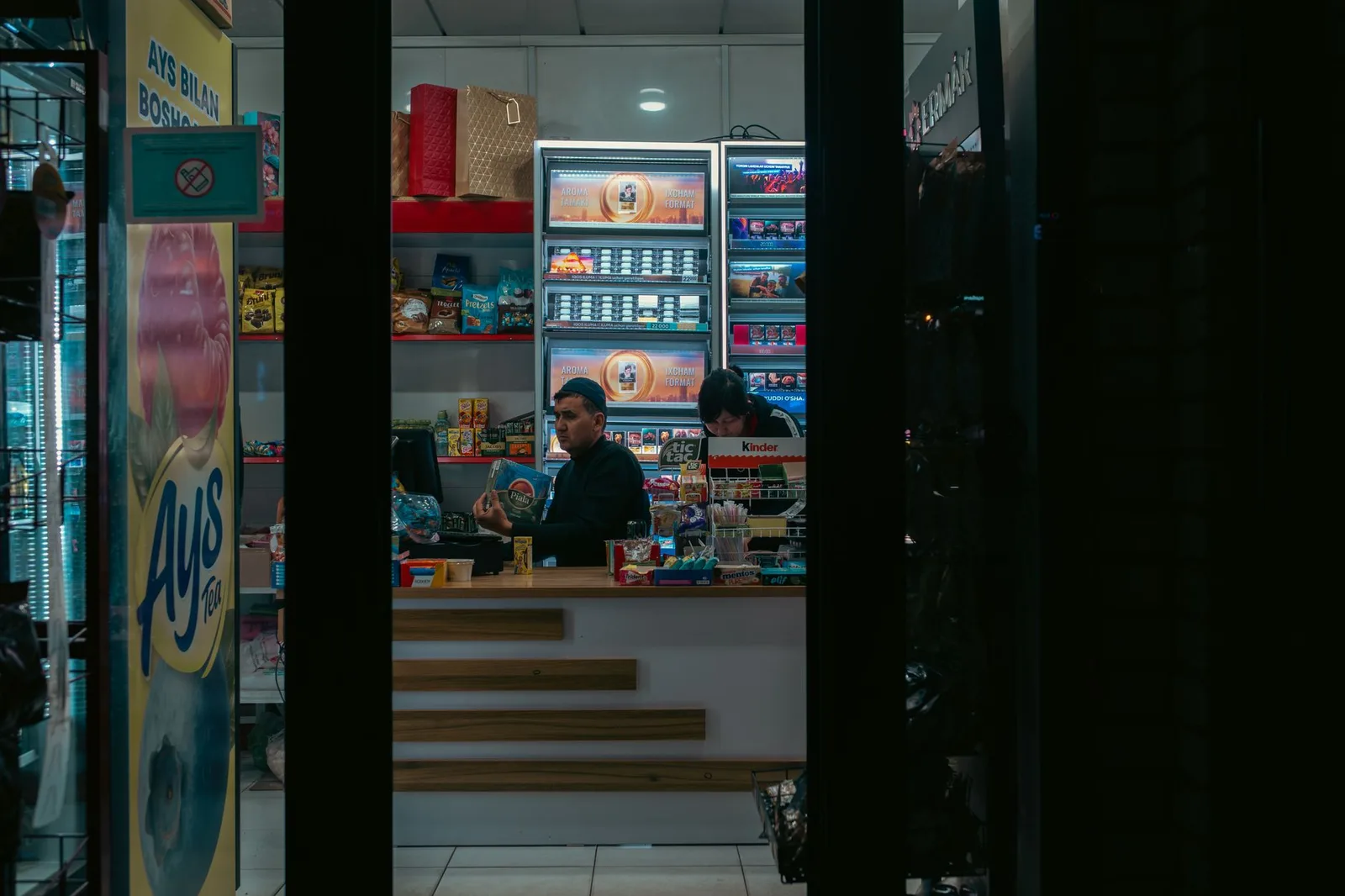Interior of a convenience store in Uzbekistan with two adults manning the counter at night.